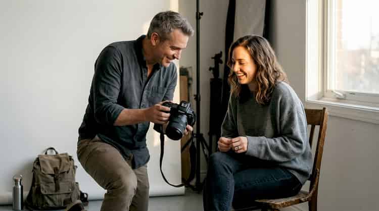 A photographer prepares his camera in the studio while a model waits ready for the session.